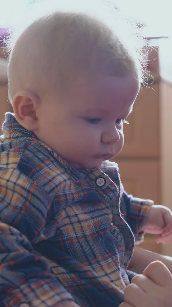 happy mother tries to button shirt of little boy sitting on bed by elder sister in light children room closeup