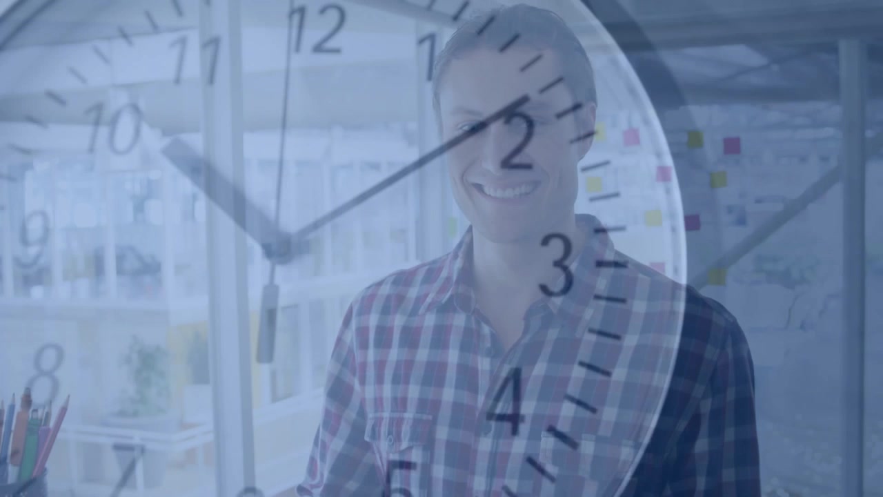 Business man typing on laptop at desk, advancing clock overlay signaling time and making him smile