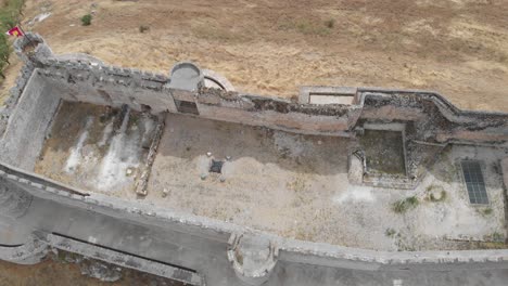 Aerial-view-over-the-ruins-of-an-abandoned-castle-structure-with-some-flags-on-its-towers