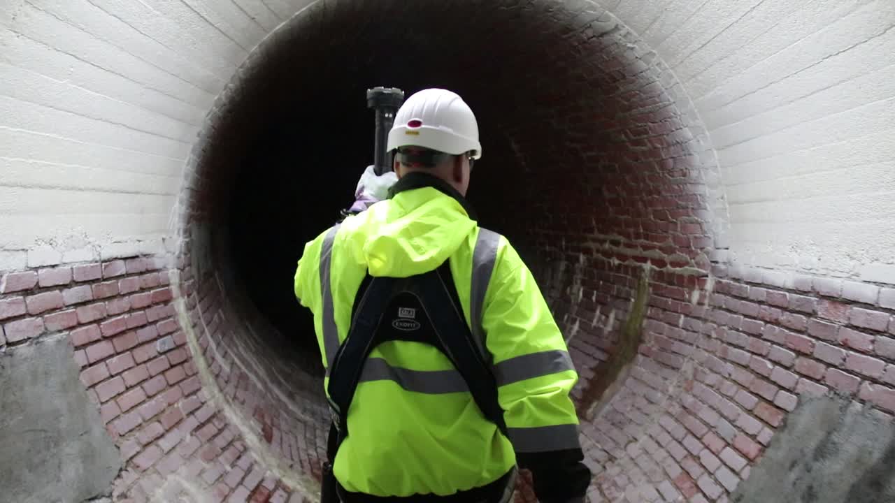 un trabajador del distrito de alcantarillado conduce el camino con una luz por un antiguo túnel de alcantarillado del siglo xix