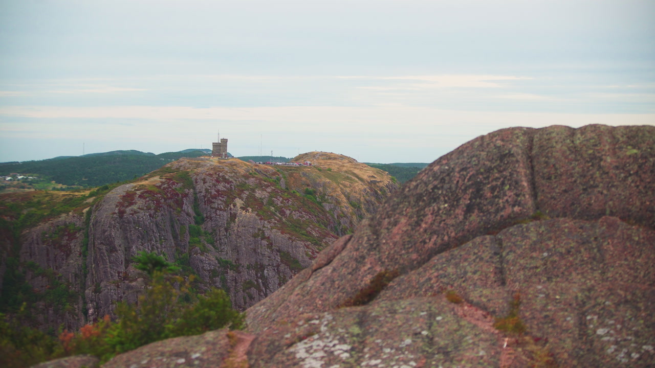 Aerial shot overlooking large mountain with castle in the distance on a cloudy fall day. Signal Hill Newfoundland, Canada