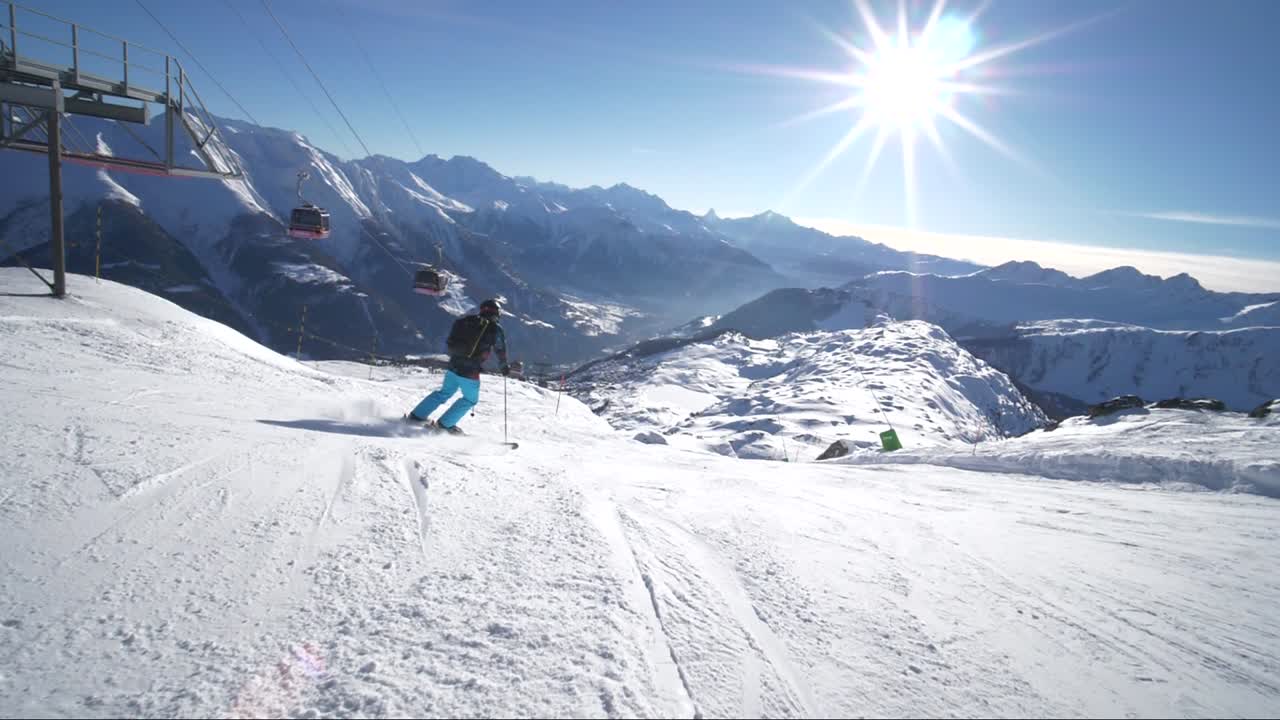 Verfolgende Zeitlupe: Ein sehr guter junger Skifahrer fährt schnelle Schwünge an einem schönen Wintertag auf einer perfekten Piste mit atemberaubender Bergkulisse in den Schweizer Alpen bei Sonnenschein.