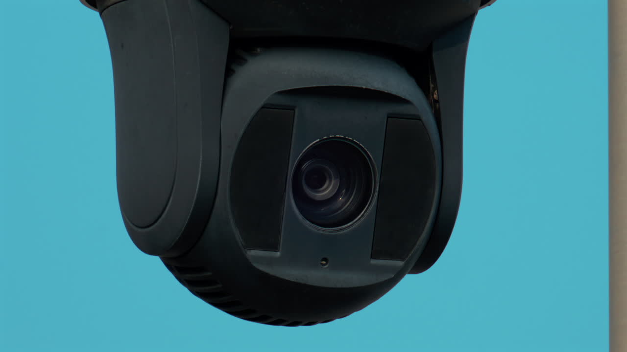 A close up of a modern black surveillance camera turning against a bright sky background