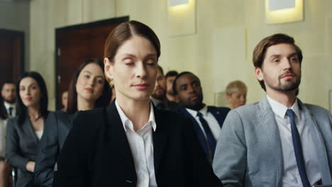 caucasian businesswoman sitting on a chair among people in a conference room and asking a question