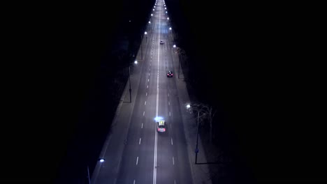 aerial view car driving on city road at dusk through dark surroundings with headlights and road lanterns