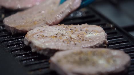 volteando bistecs medio raros en una plancha de metal con especias y aceite, tiro estático en cámara lenta