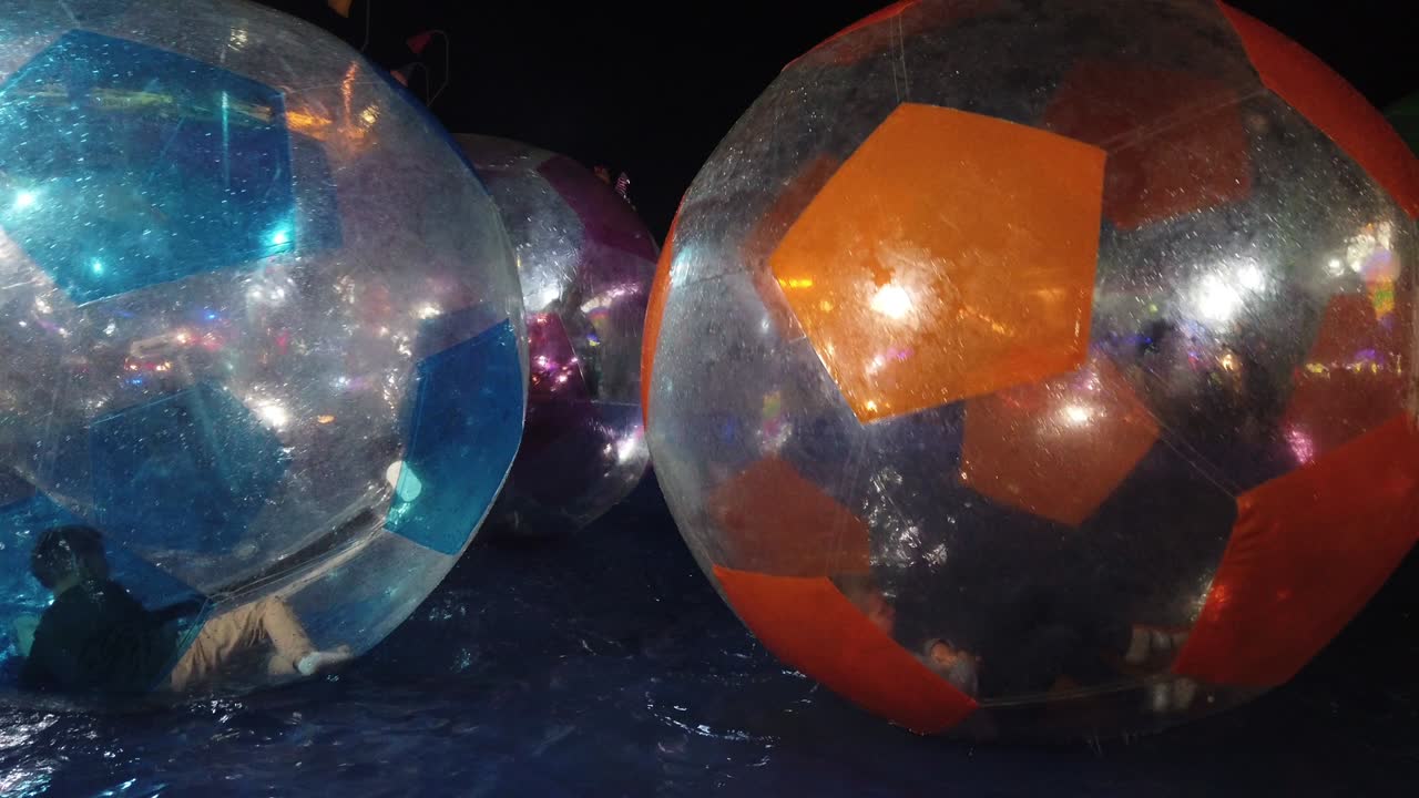 niños no identificados juegan divirtiéndose dentro de grandes bolas transparentes en el agua por la noche