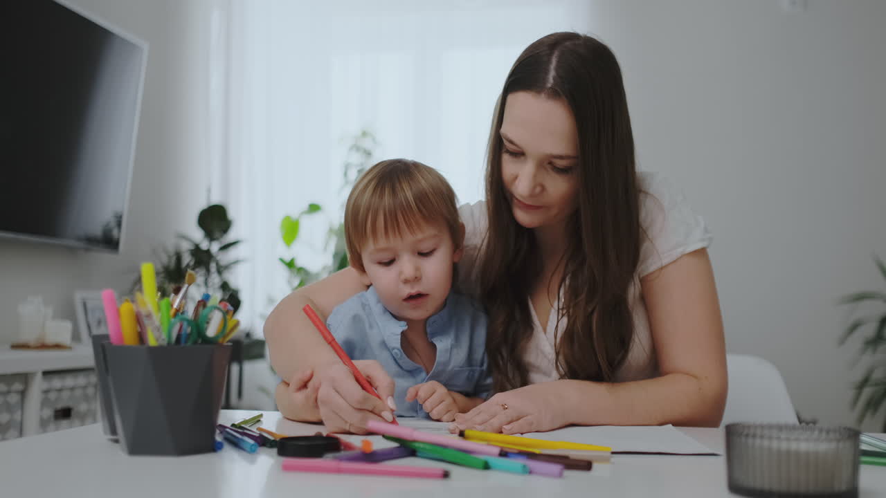 una familia de dos niños y una joven madre sentada en la mesa dibuja en papel con lápices de colores. desarrollo de la creatividad en los niños.
