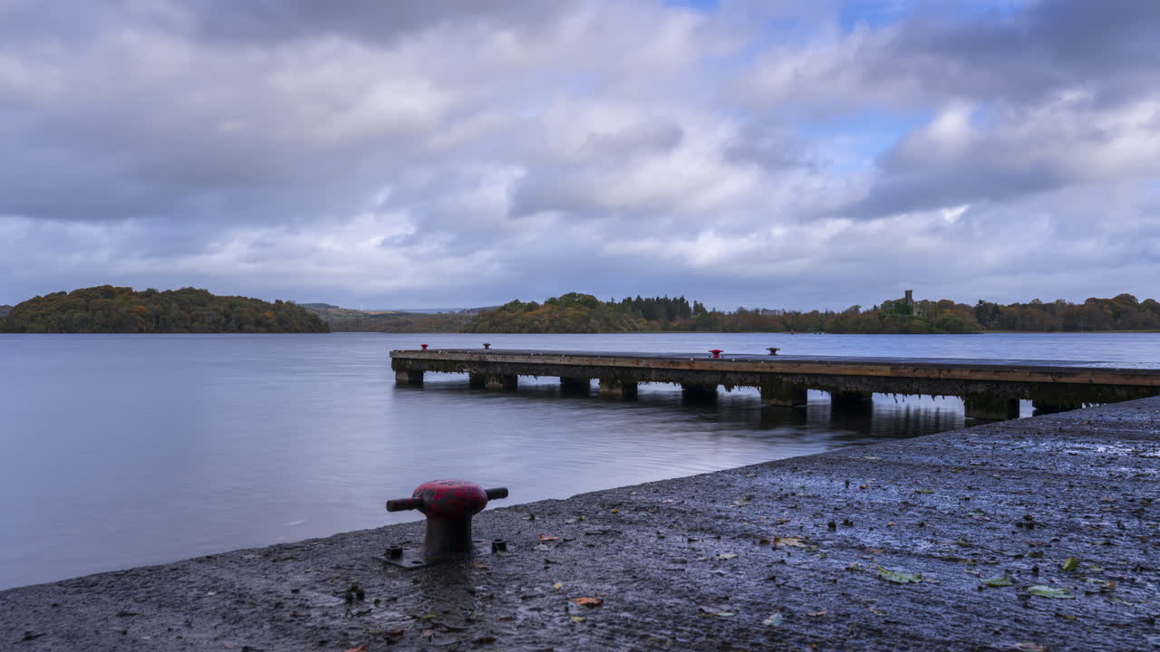 Timelapse di un'area con molo in cemento sul lago con una foresta in lontananza in una giornata prevalentemente nuvolosa a Lough Key nella contea di Roscommon in Irlanda.