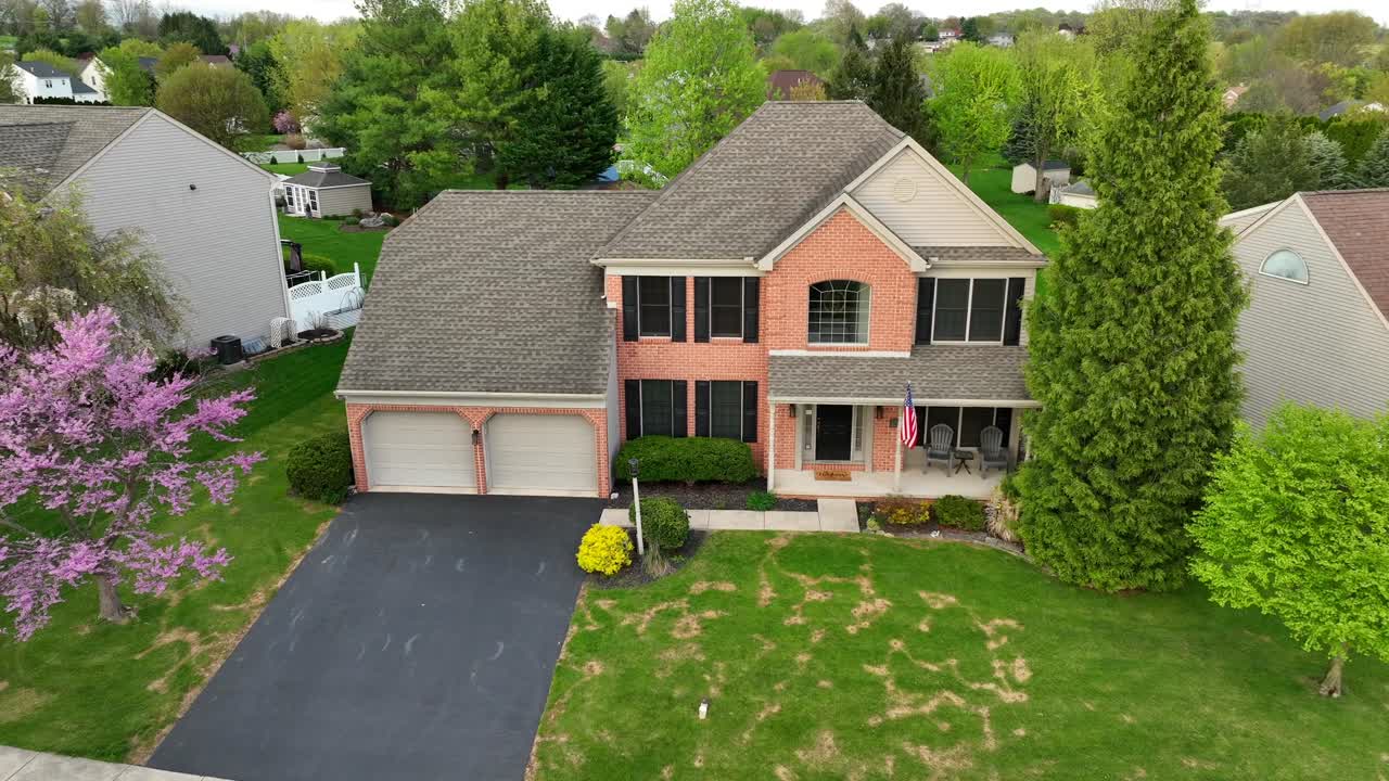 Large middle class home with American flag and blooming trees in spring. Aerial establishing shot in neighborhood.