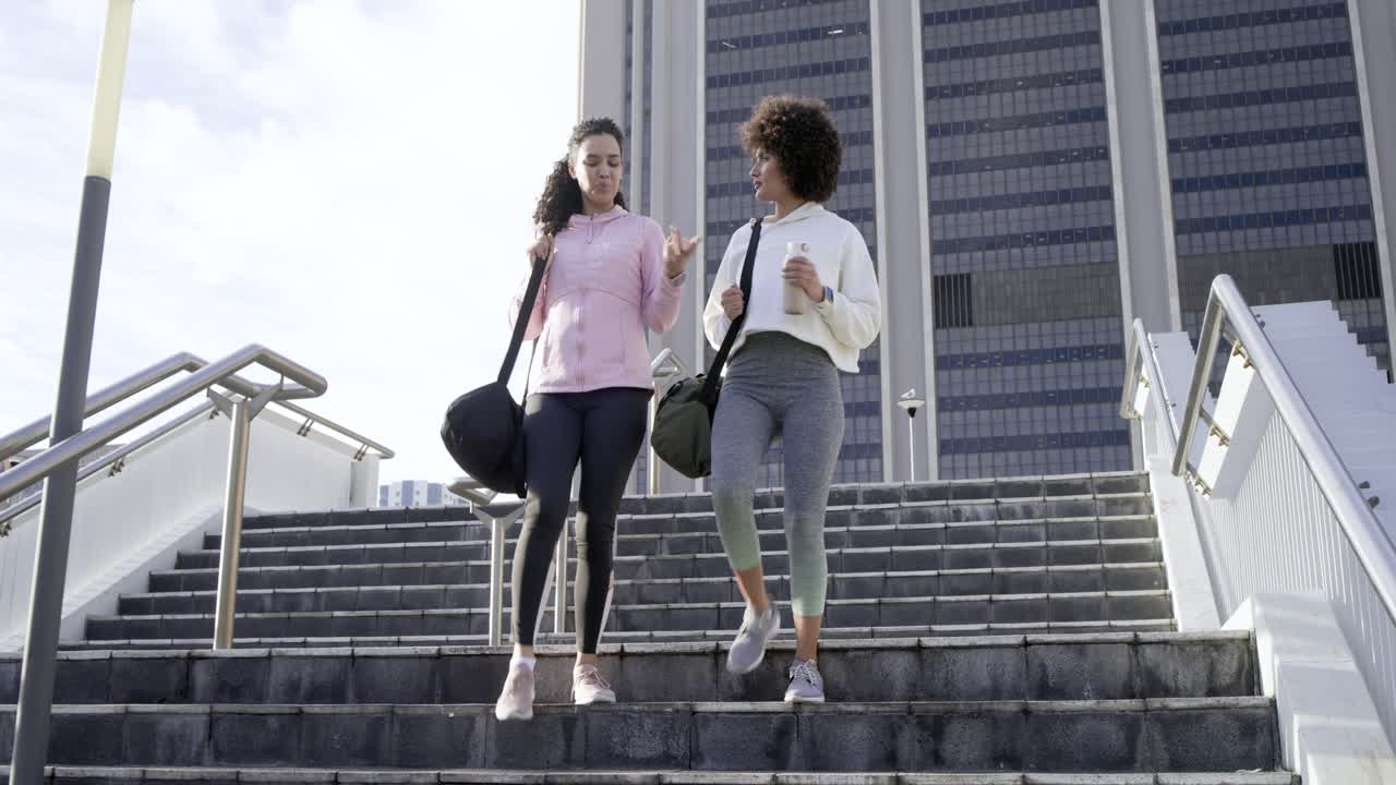 At clip start, Diverse female friends walking down urban stairway planning workout with duffel bags