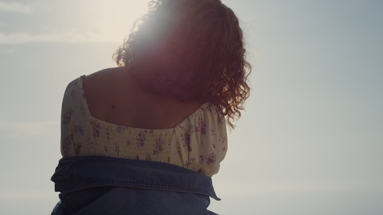 chica desconocida de pie hacia atrás en la playa disfrutando de la brillante luz del sol de la tarde.