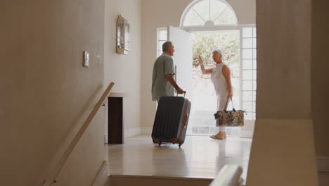 senior couple with suitcase opening front door and leaving for vacation