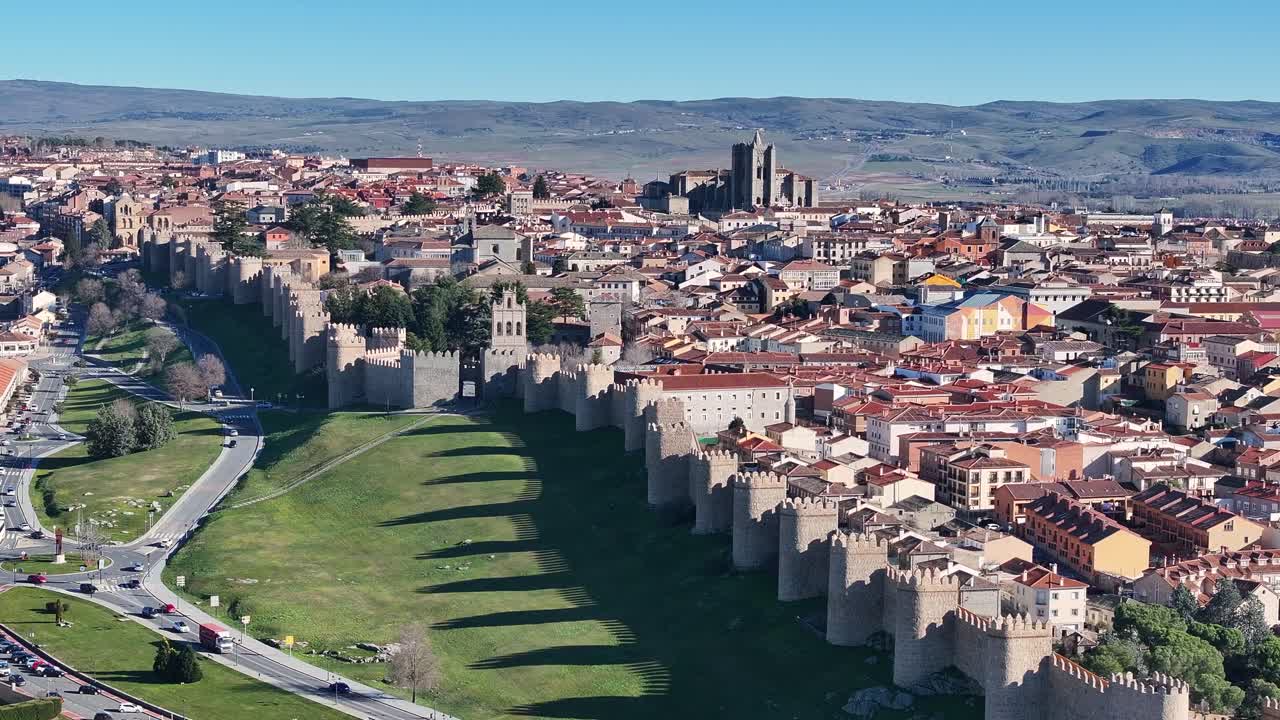 na tela norte da cidade murada de ávila, vendo dentro da catedral e suas casas, vemos a sombra da parede projetada na grama e uma estrada com carros circulando na espanha.