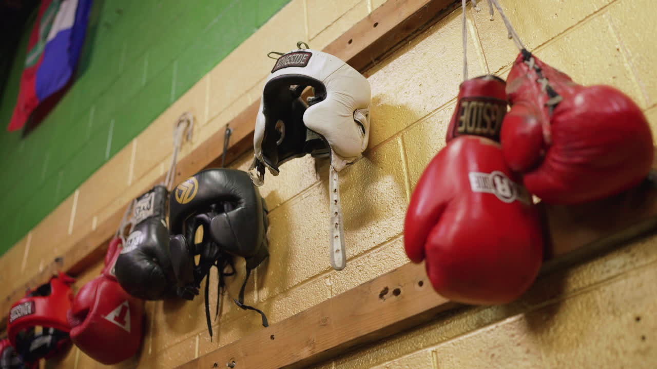 una toma estática de un gimnasio de boxeo donde también se ven algunos pares de guantes de boxeo de colores colgados y algunos protectores de cabeza