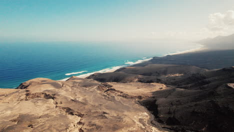 Vista-Aérea-Del-Espectacular-Paisaje-Costero-De-Fuerteventura,-Vista-Panorámica-De-La-Playa-De-Cofete-En-El-Fondo-Con-Azul-Océano-Atlántico