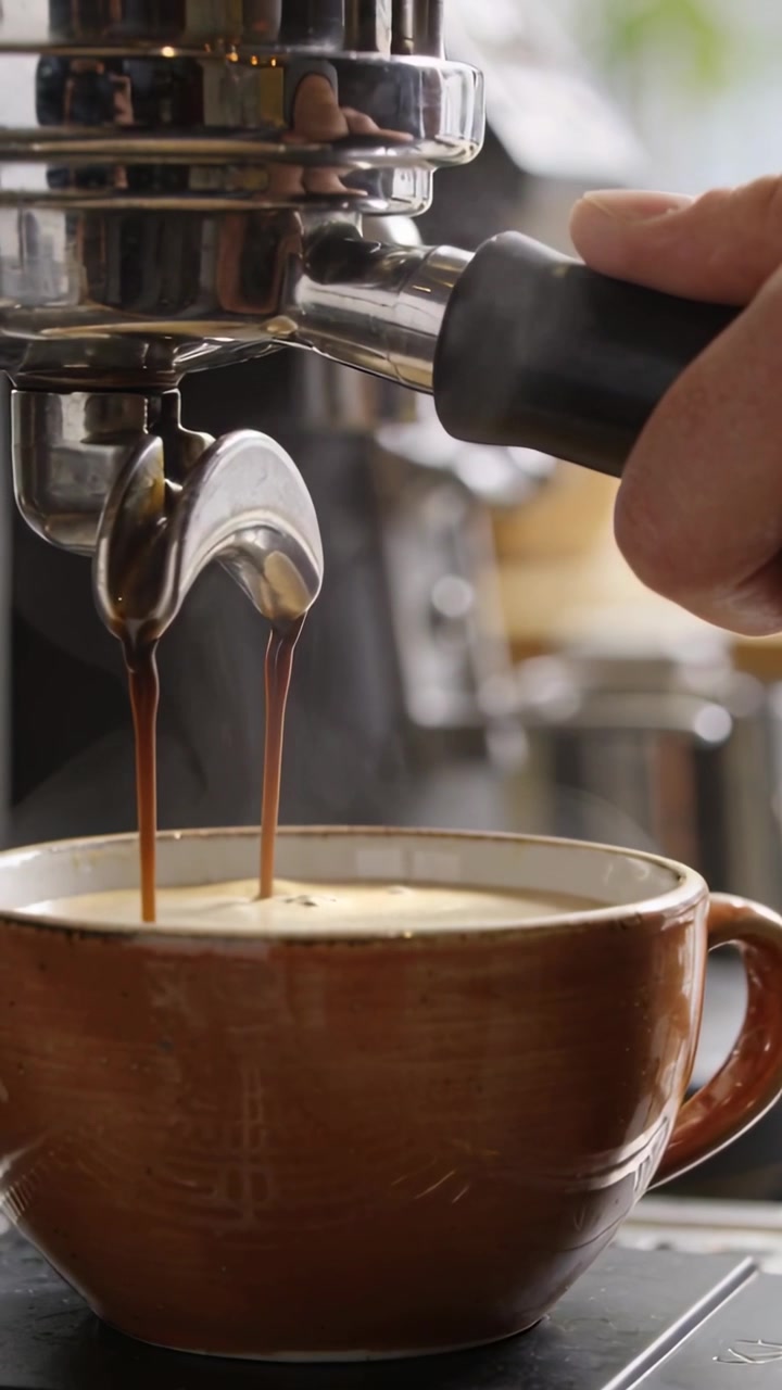 Video verticale: Barista che blocca il portafiltro ed estrae l'espresso in una tazza al bancone, formando la crema.