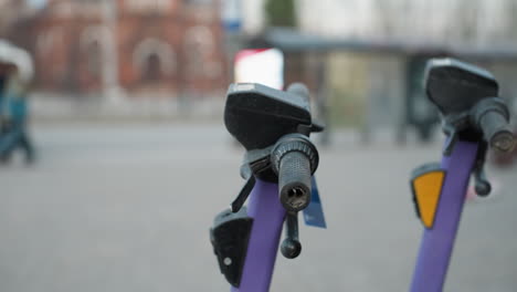 close view of purple electric scooters parked in a busy urban area, the background includes blurred details of a cityscape with moving cars and people