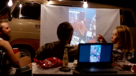 friends watching video with projector in campsite