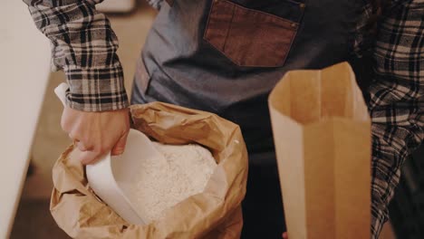 Baker-dumping-flour-from-a-sack-into-a-carton-bag-in-slow-motion