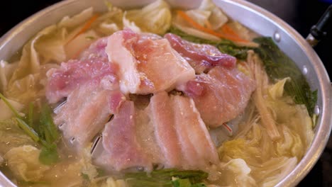 steaming hot pot filled with thinly sliced meat and loads of vegetables, cooked on a stove top using induction heat