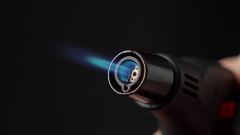 butane torch lighter with blue flame and black background, close up shot