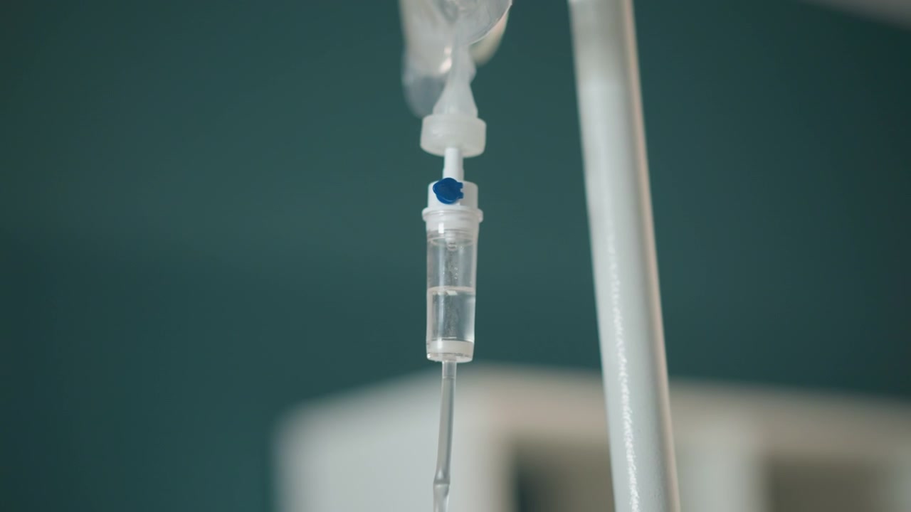 Perfusion intraveineuse suspendue à l'intérieur d'une ambulance, le secouriste fixe le tube et la pince pendant le transport d'urgence, gros plan sur la chambre de goutte à goutte et le flux de solution saline, moniteur portable et civière flous en arrière-plan