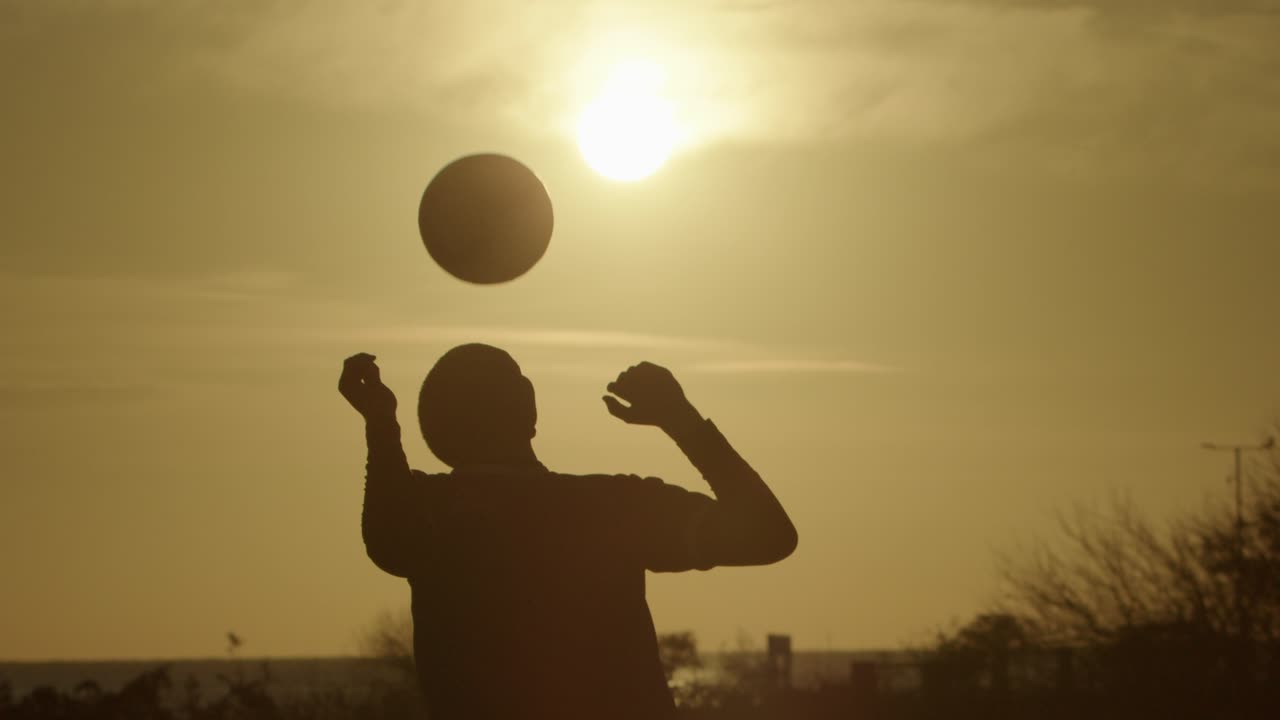 A person practices ball skills in the sunset, with a glowing sky in slow motion