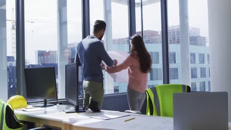 Two-diverse-male-and-female-colleagues-looking-at-architectural-blueprints-and-talking