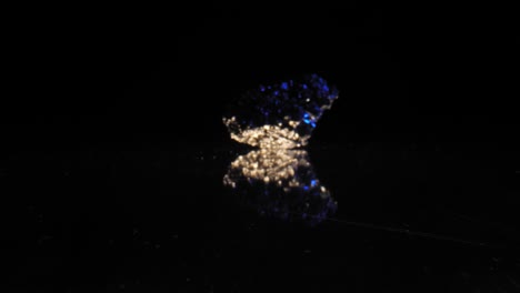 quartz crystal shimmering in blue light against dark background, captured through smooth zoom-in dolly, reflections underneath