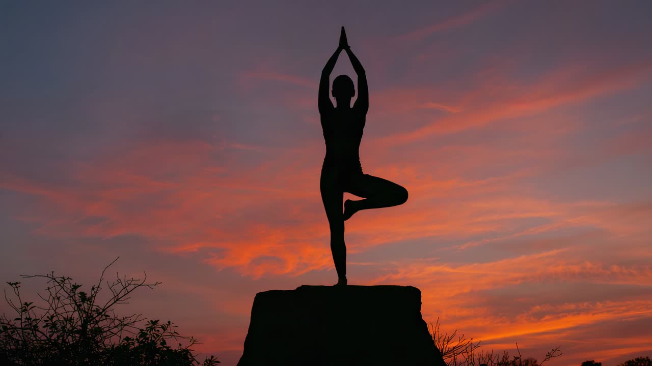 Holding tree pose yogi in activewear adjusting balance as sunset light shifts on rock with shrubs