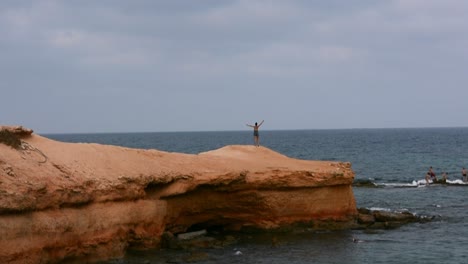 Una-Niña-Grita-Y-Extiende-Sus-Brazos-Alegremente-En-Un-Acantilado-Junto-Al-Mar,-En-La-Costa-Mediterránea