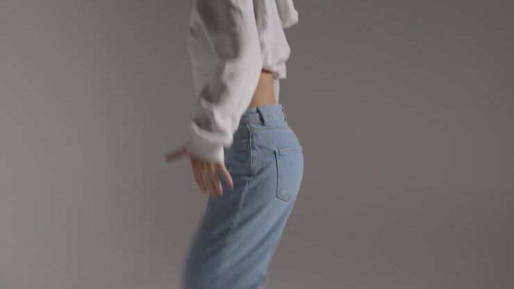 Studiebillede af ung kvinde, der danser og har det sjovt mod grå baggrund