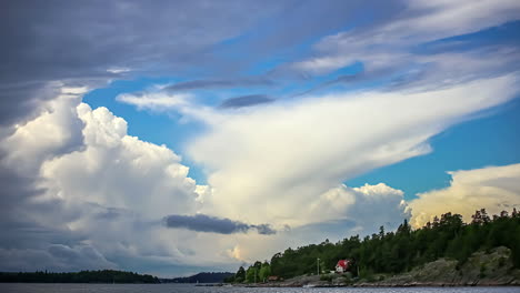 Statische-Ansicht-Eines-Sees-Und-Eines-Weißen-Hauses-Zusammen-Mit-Dichtem-Grünen-Wald-In-Einer-Ländlichen-Sommerlandschaft-Mit-Weißen-Wolken,-Die-Im-Zeitraffer-Vorbeiziehen