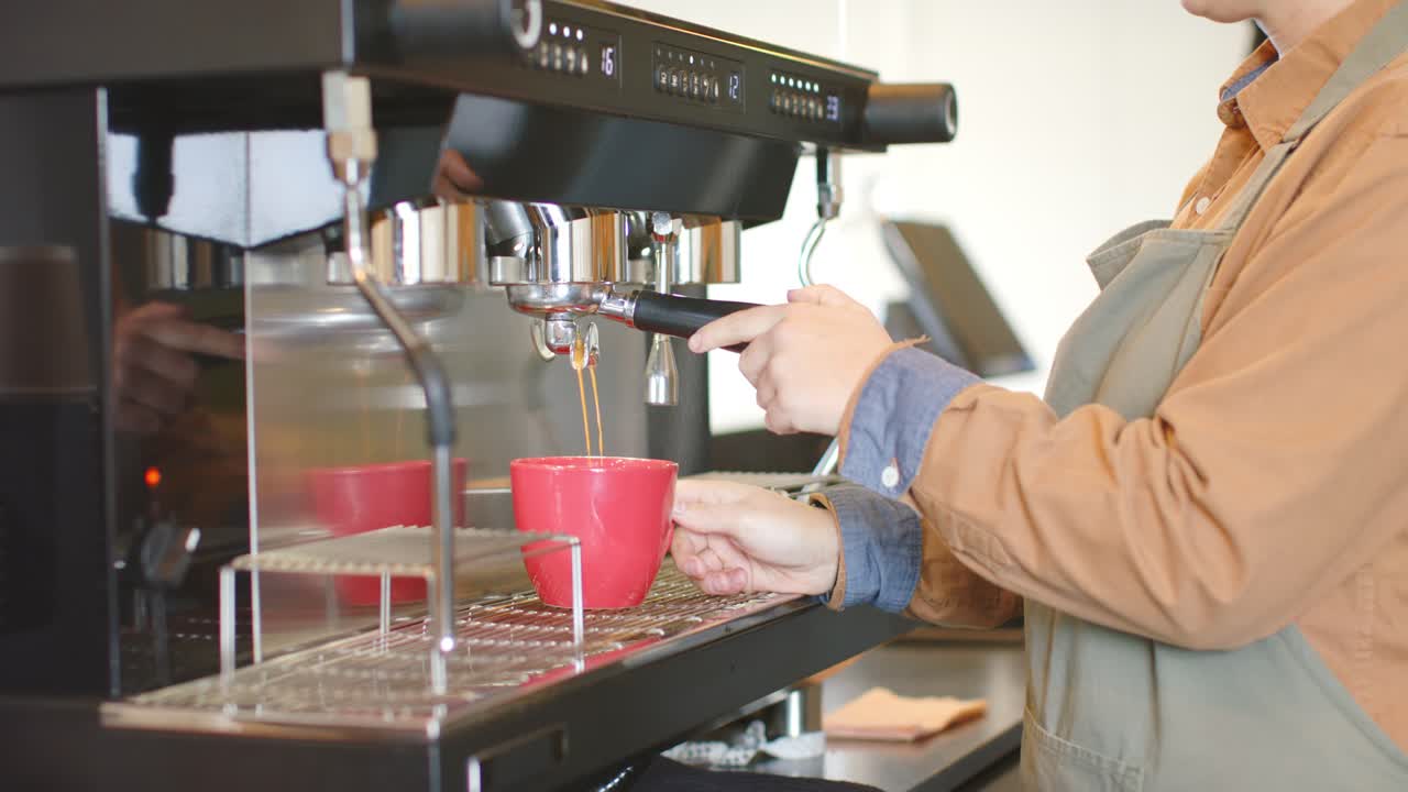 Barista preme il pulsante della macchina per l'espresso, versa un caffè nella tazza al bancone e controlla la crema