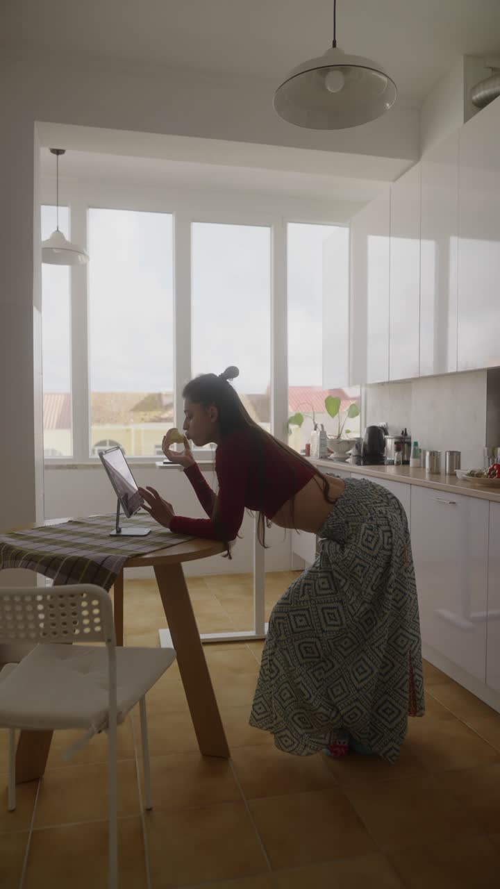 Donna che mangia frutta mentre è in videochiamata nella sua cucina moderna