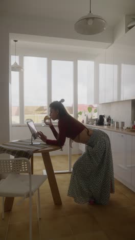 woman eating fruit while on a video call in her modern kitchen