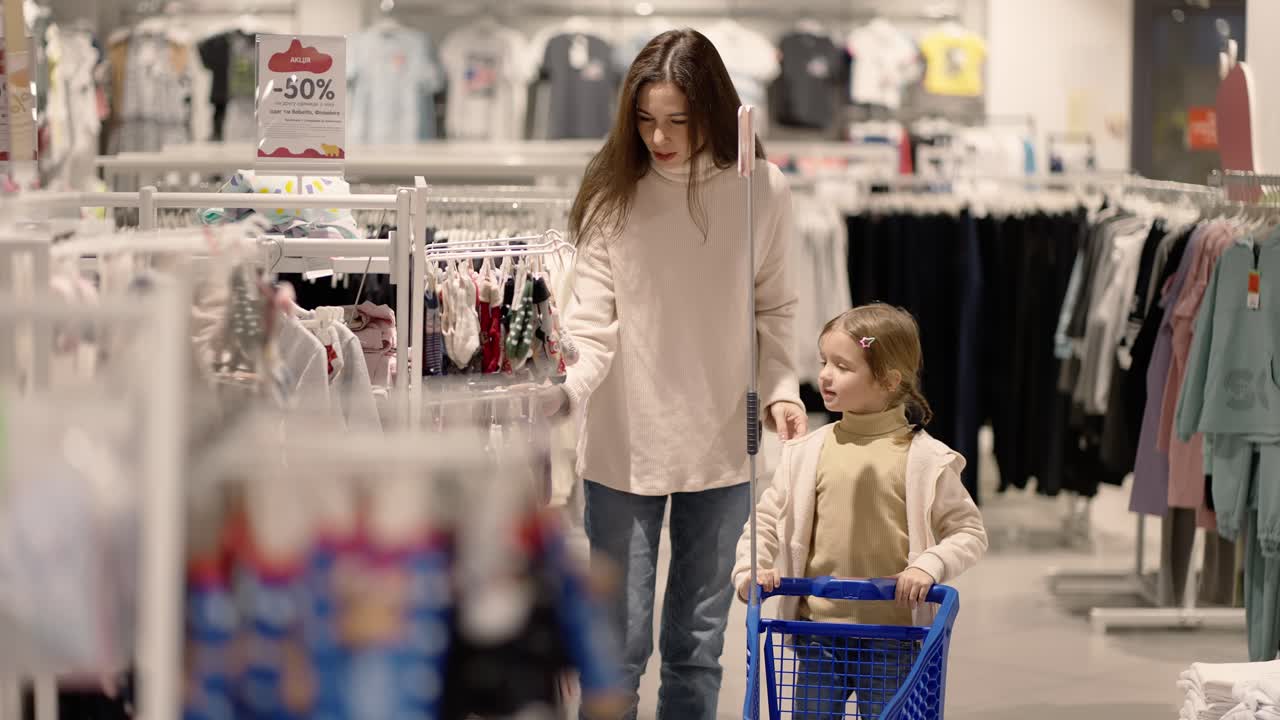 madre e hija caminando por una tienda de ropa con un carrito de compras para niños