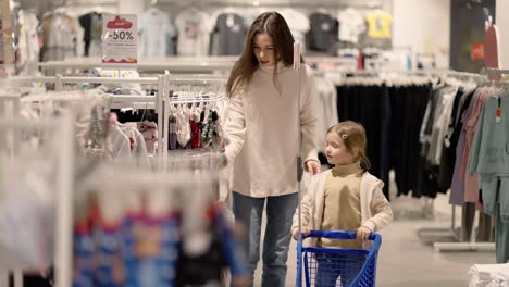 mother and daughter walking through a clothing store with children shopping cart