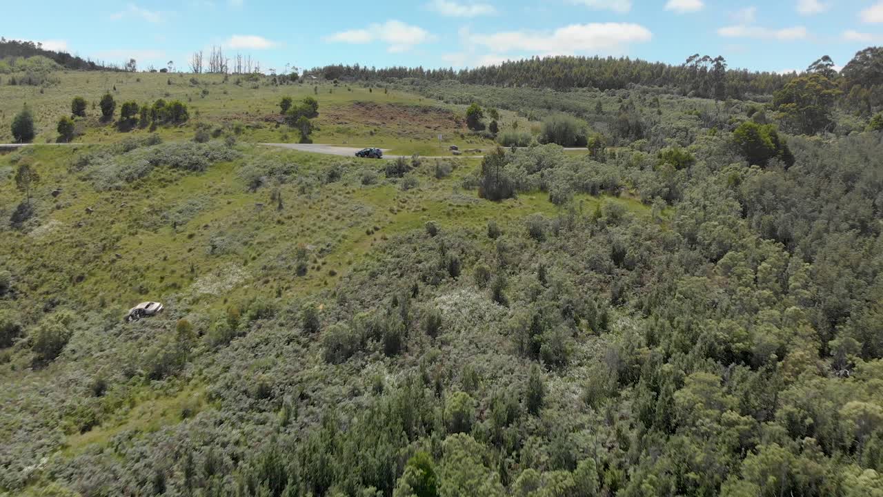 toma aérea de un automóvil estacionado en un mirador de montaña con los restos de un automóvil en la ladera de la montaña