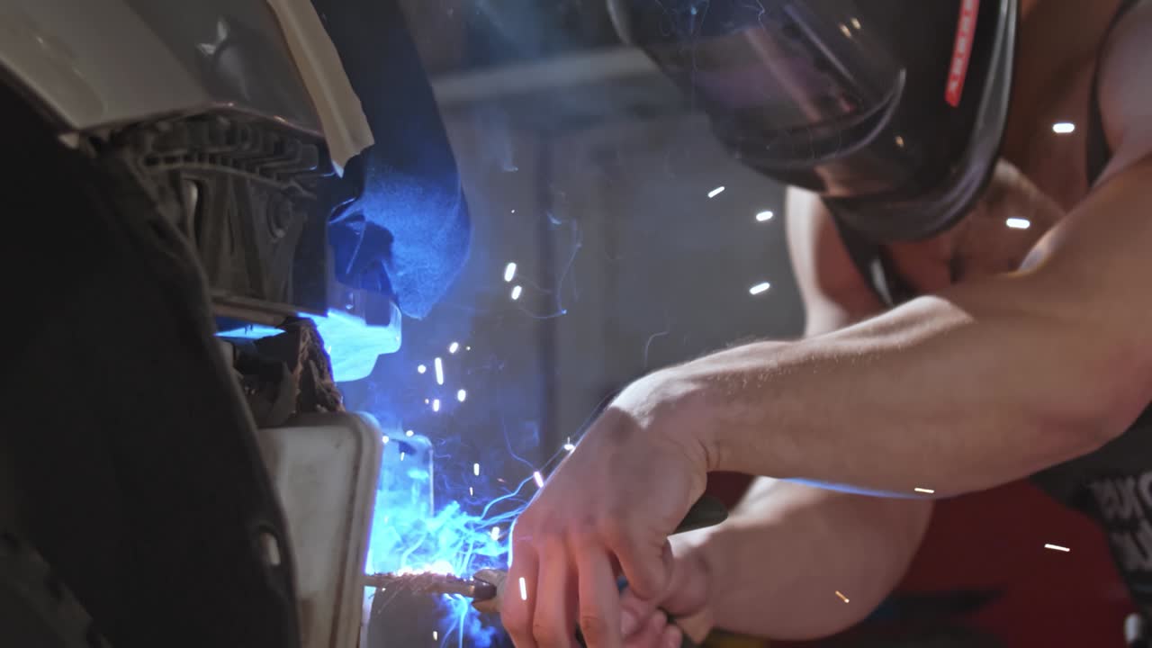 Welder sexy mechanic dancing naked doing sparks on a car metal body, in a mask with big muscular biceps, 50 fps ready for slow motion