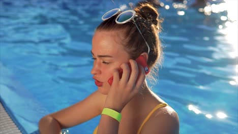 teenage girl talking on phone by a pool