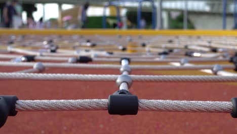 climbing net in the park. game equipment for children. focus is on the front. the background is parents and children. the subject is in the middle.