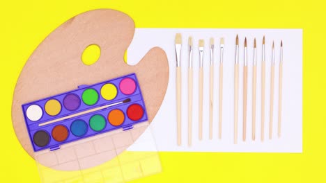 art tools for drawing and painting and water colors appear on white paper on yellow theme. stop motion