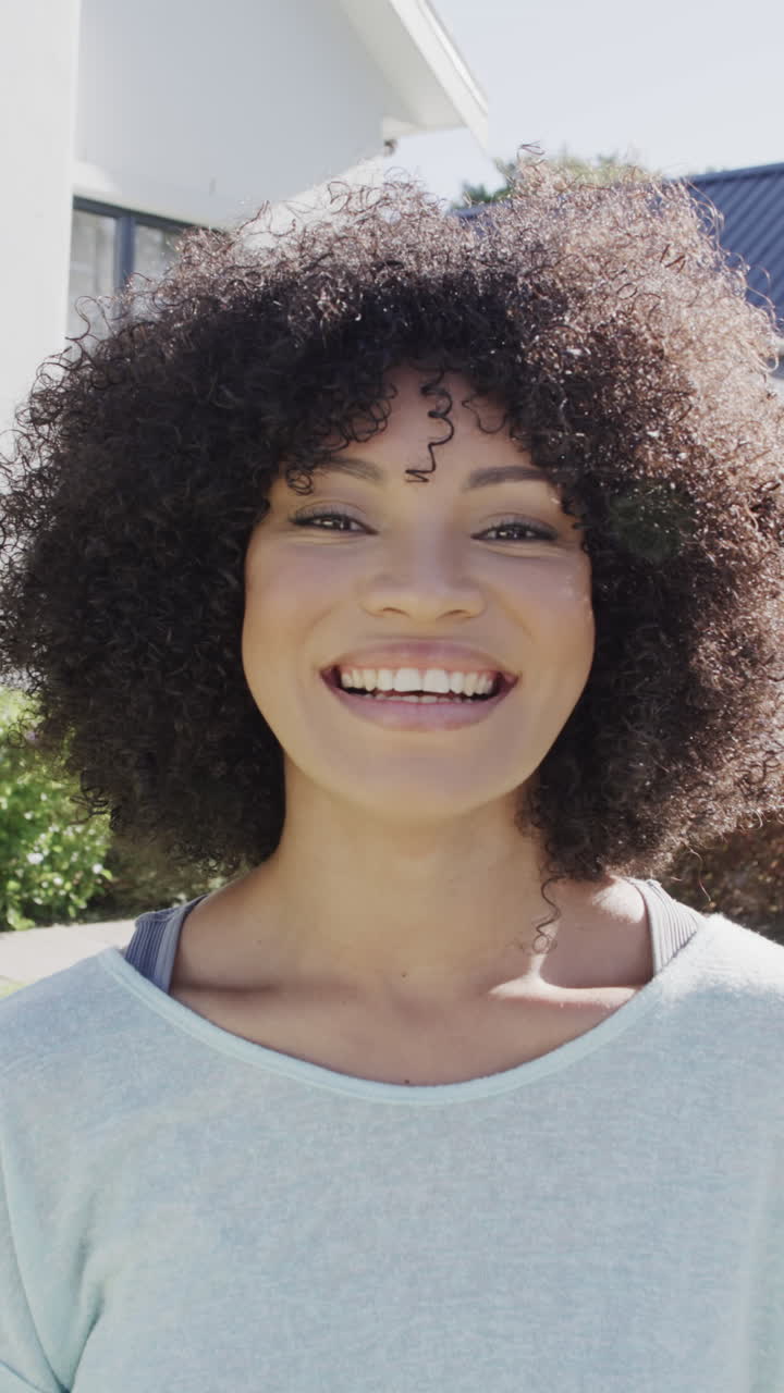 Vertical video of portrait of happy biracial woman smiling in garden, slow motion