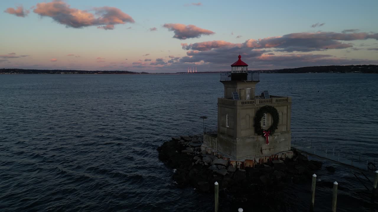 una vista aérea de ángulo bajo del faro del puerto de huntington en long island, nueva york al atardecer, con una corona de navidad en él
