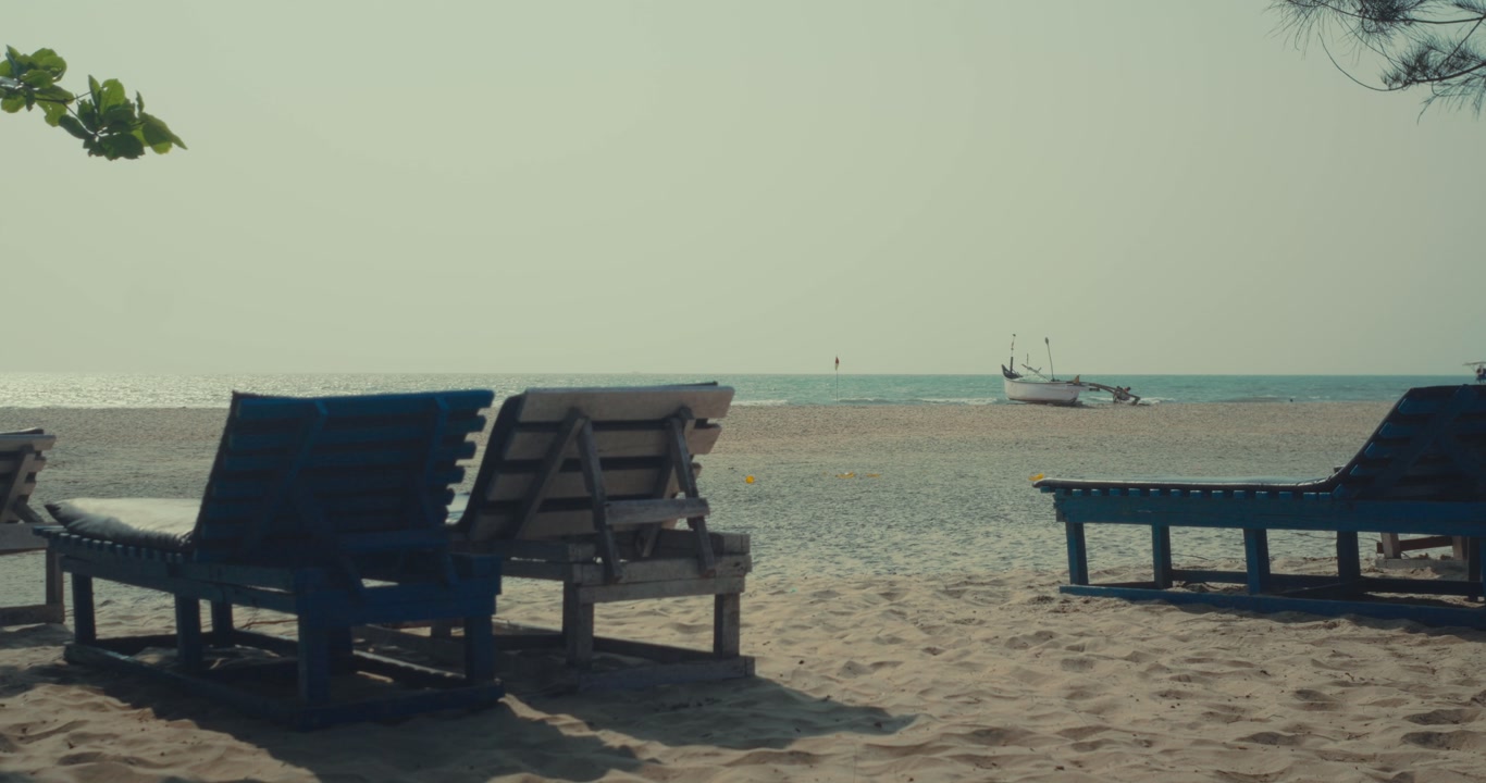 Empty beach chairs on sand facing ocean with small fishing boat in distance calm coastal travel scene