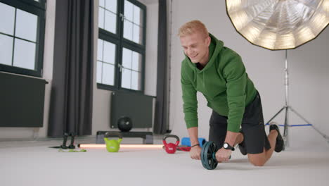 Young-caucasian-male-on-knees-working-out-on-floor-with-ab-roller