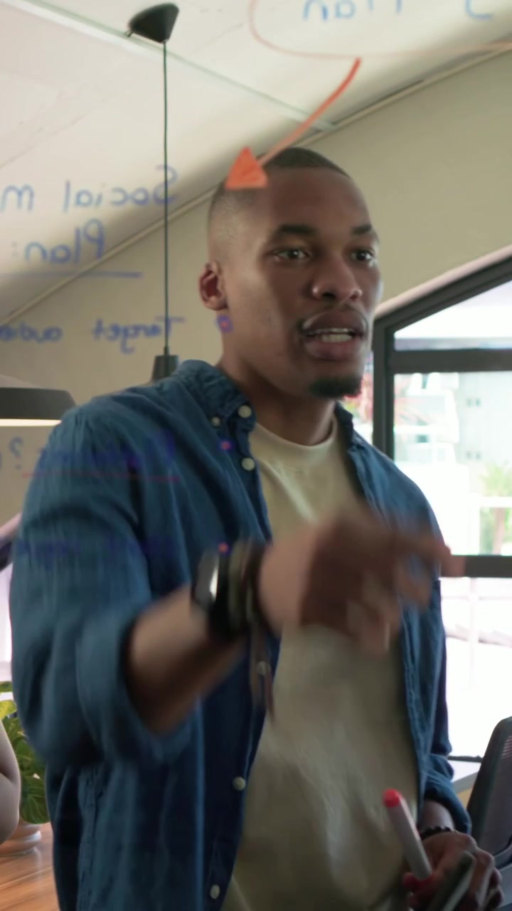 Vertical video: Marking glass man in blue shirt writing after woman leading planning with markers