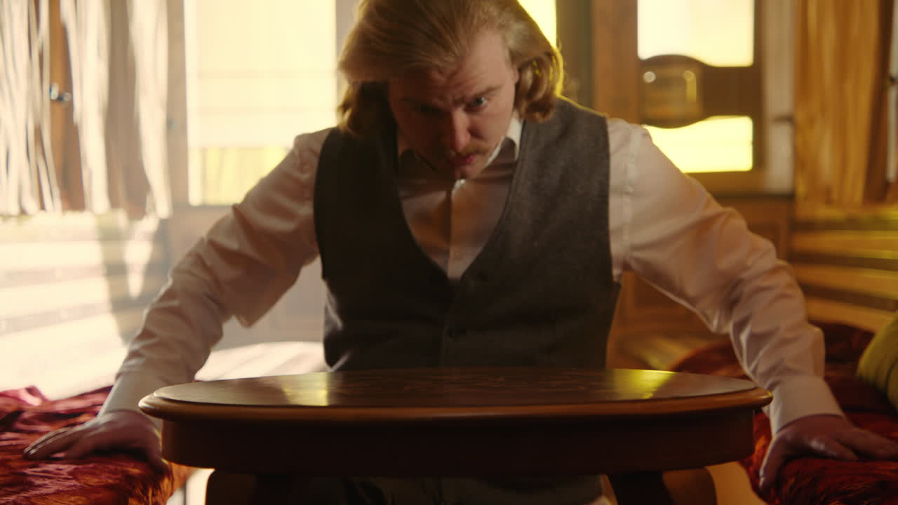 Man in vintage clothing looking at a wooden table in a train car